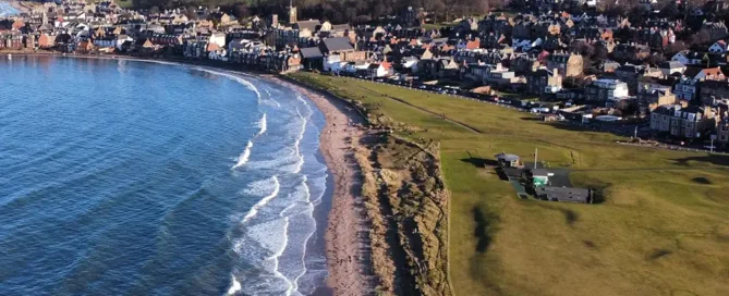 Aerial view looking out over North Berwick town and golf course with waves crashing onto the shore. North Berwick Scotland.