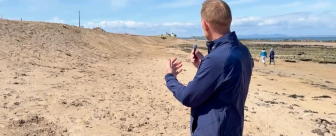 Stuart Bayne filming a coastal erosion update on North Berwick's West Sands beach beside a reshaped dune bank